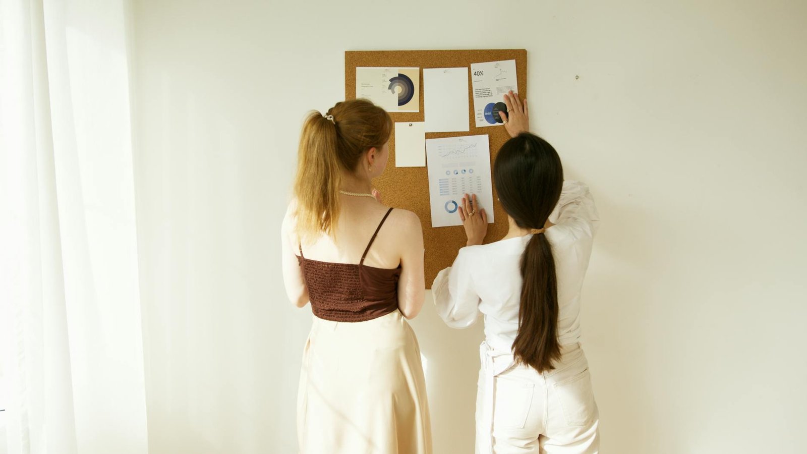 a pair of women comparing the graphs posted on corkboard